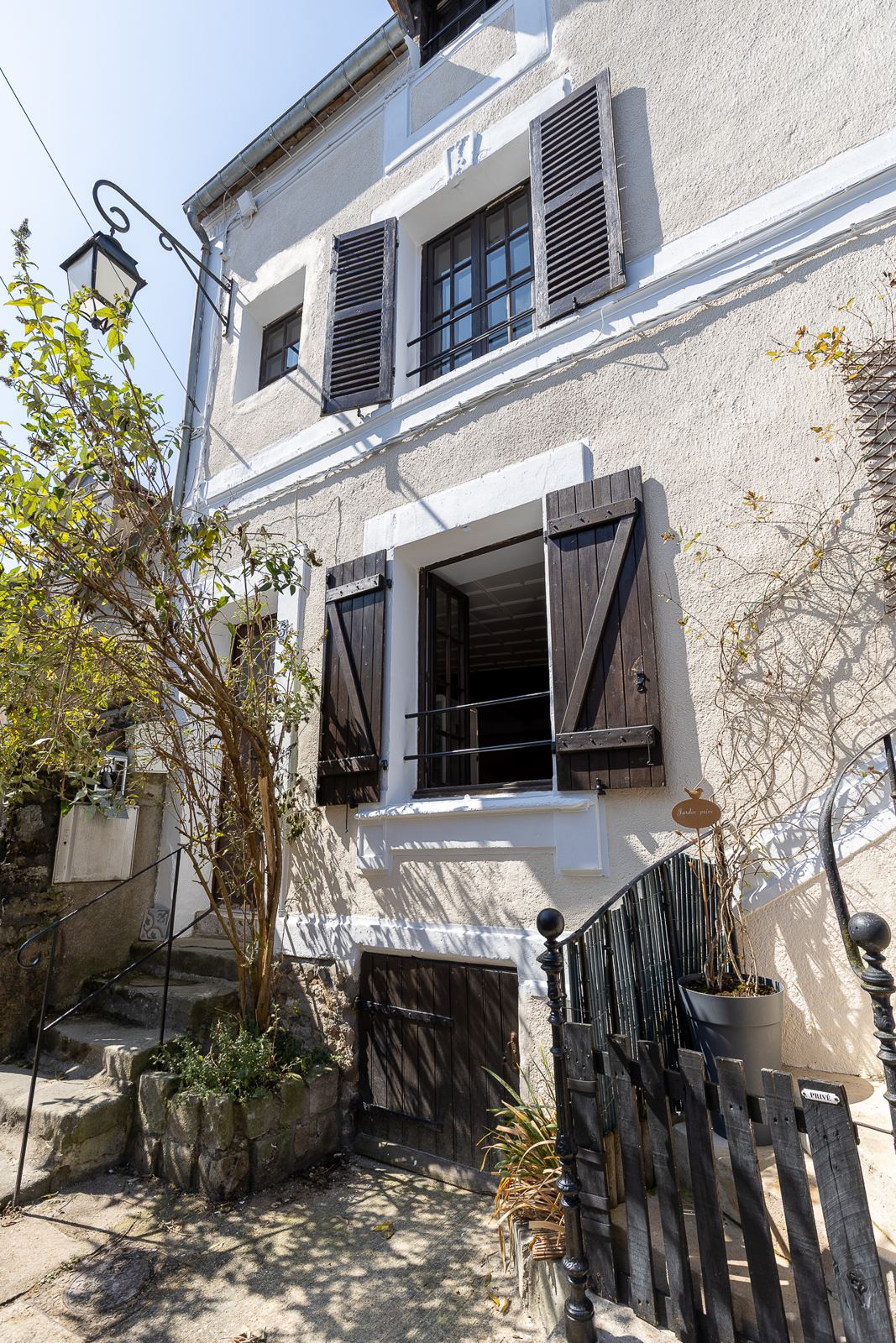 Façade de la maison : volets en bois sombre, réverbère en fer forgé et petit escalier de pierre