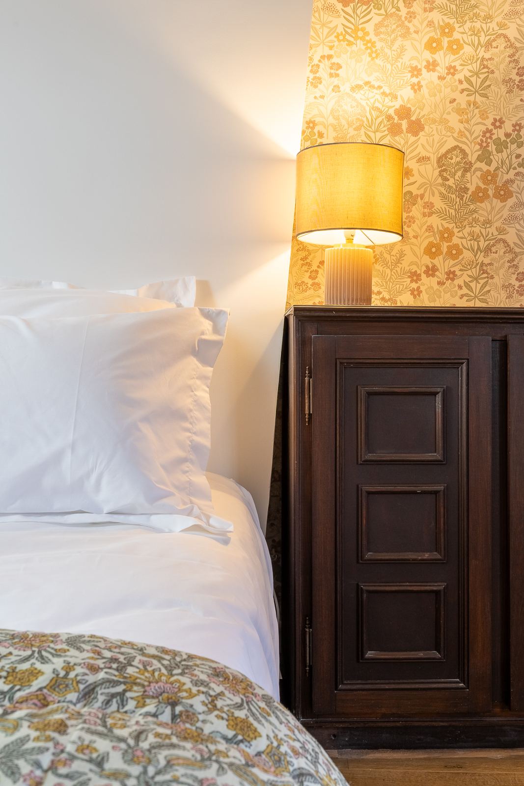 Lampe de chevet allumée devant un papier peint fleuri