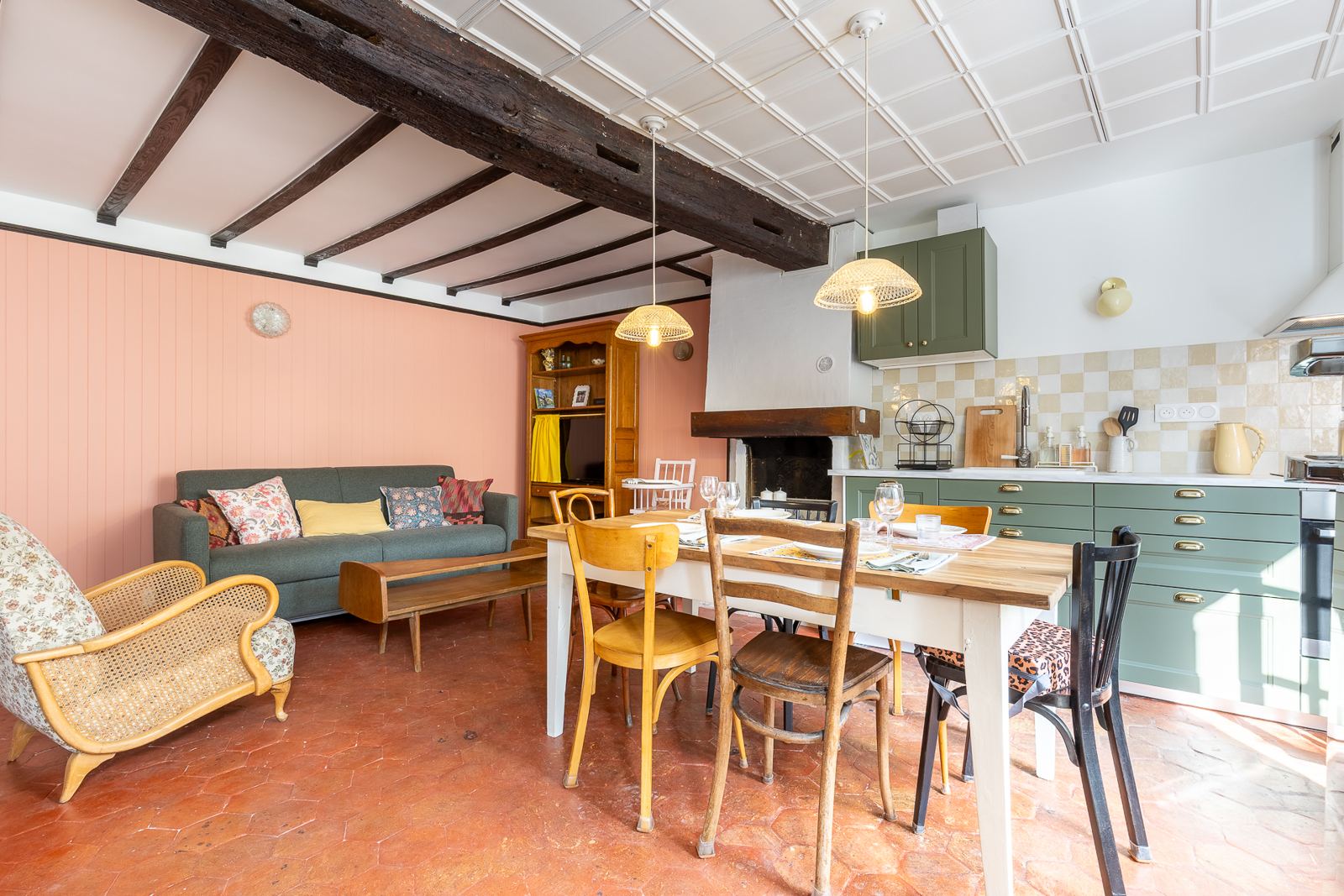 La grande table et ses chaises de bistrot dépareillées, devant la cuisine vert sauge